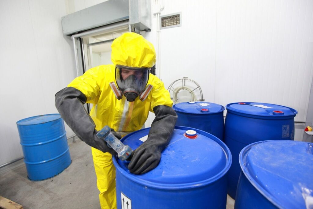 Worker in protective hazmat suit handling chemical drums in a safety-controlled environment