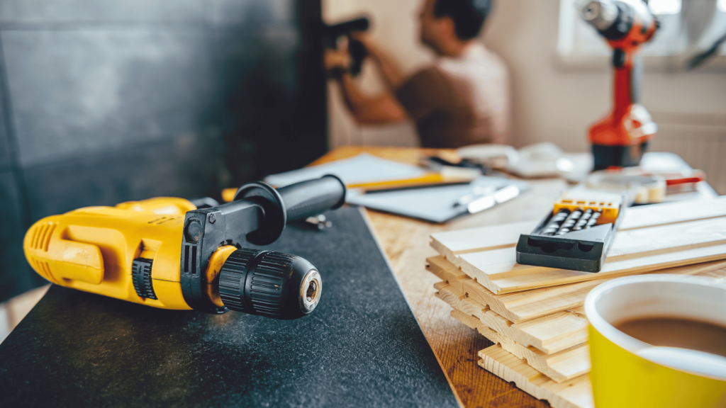 A focused workspace with a vibrant yellow power drill in the foreground on a black surface.